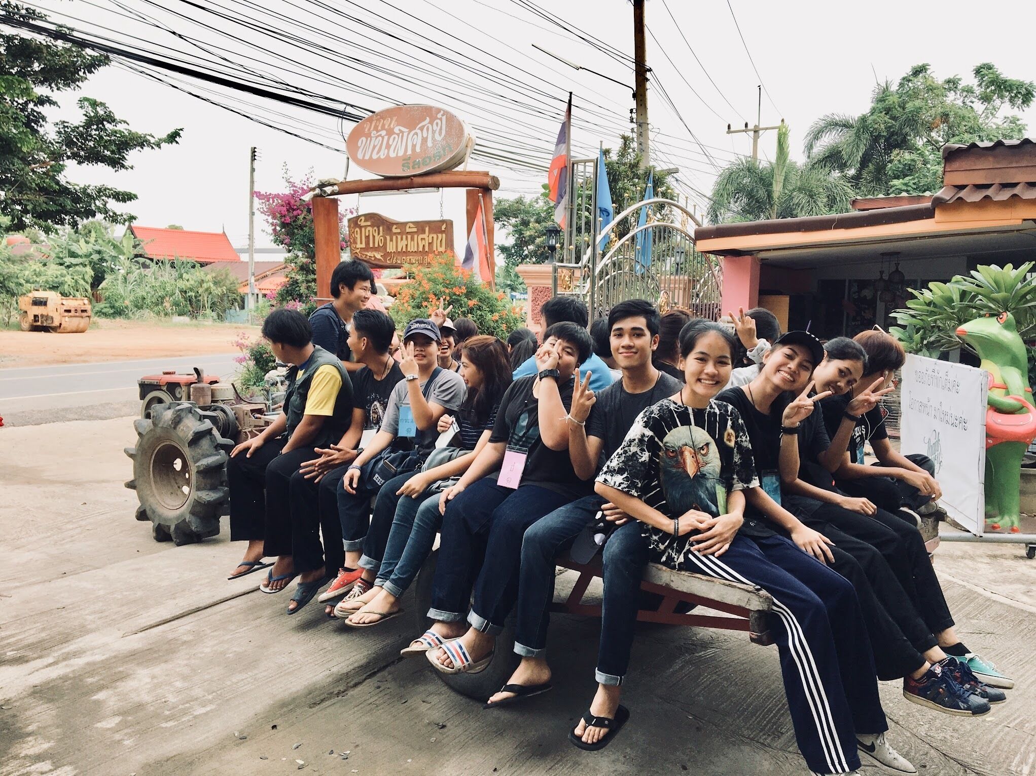 A group of people sitting on a bench outside a building with a signboard.