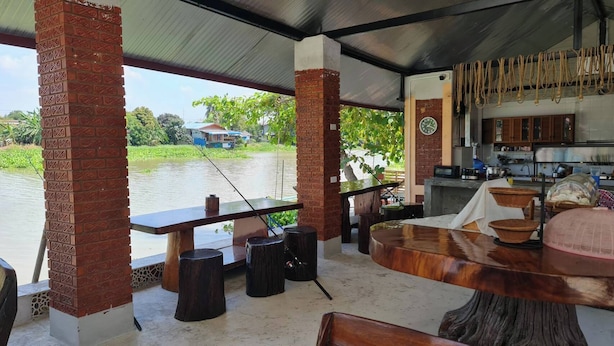 Een eetgedeelte aan de rivier met een houten tafel en stoelen, een vishengel en een keuken met een klok.