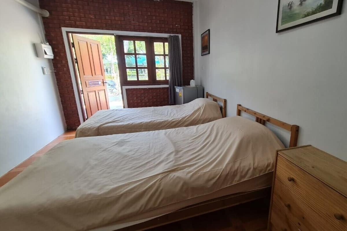 Une chambre avec deux lits, une commode en bois, un radiateur et une fenêtre donnant sur un paysage verdoyant.