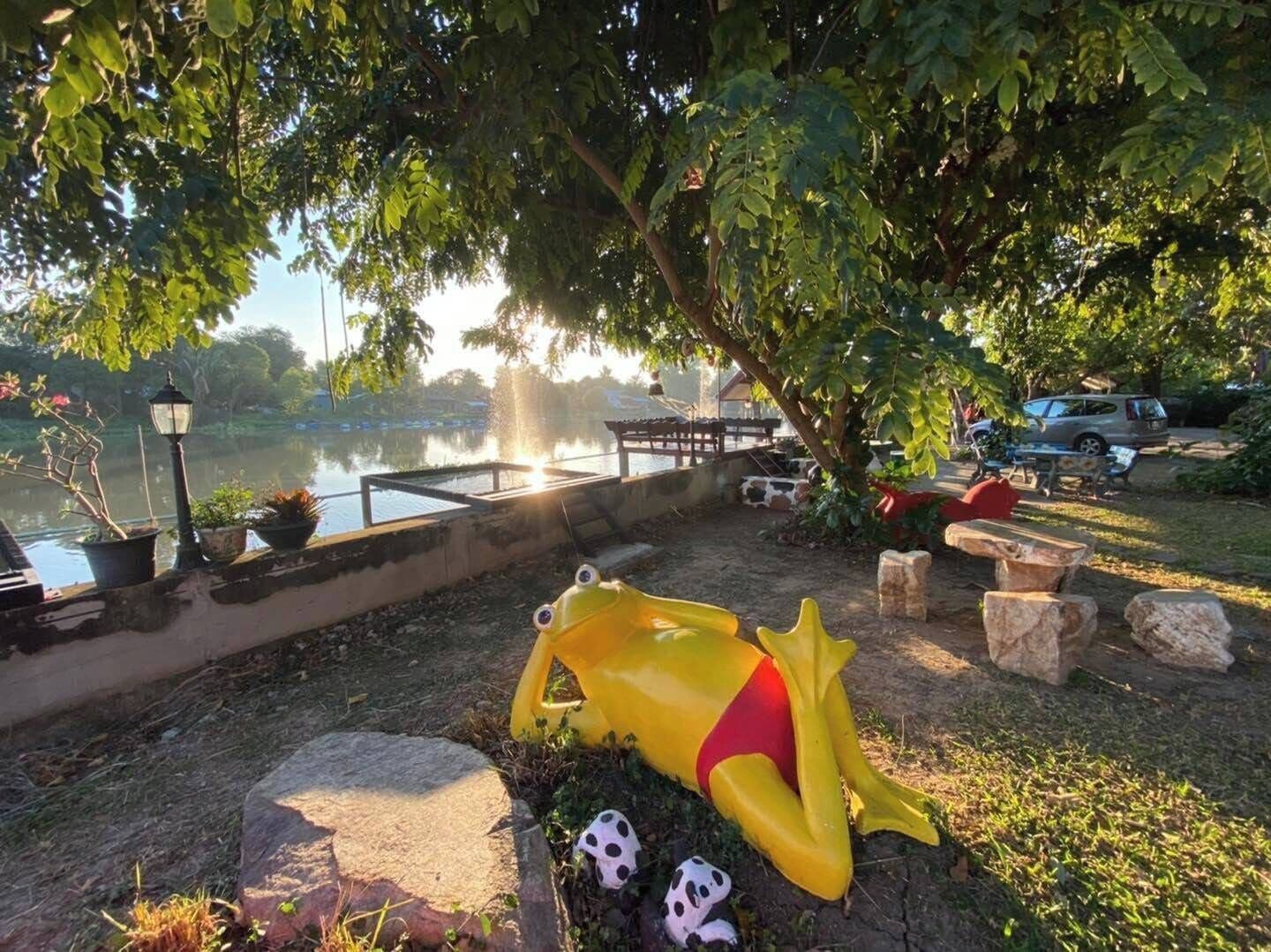 Un parque con un estanque, una escultura de un sapo amarillo y un farol.