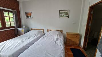 Ein Zimmer mit zwei Einzelbetten, einem kleinen Holzkommode, einem Heizkörper und einem Fenster mit Vorhängen.