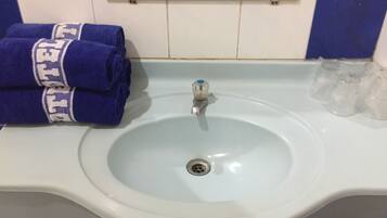 A bathroom sink with a mirror above it, a towel rack with folded towels, and a row of clear glasses on the sink's edge.