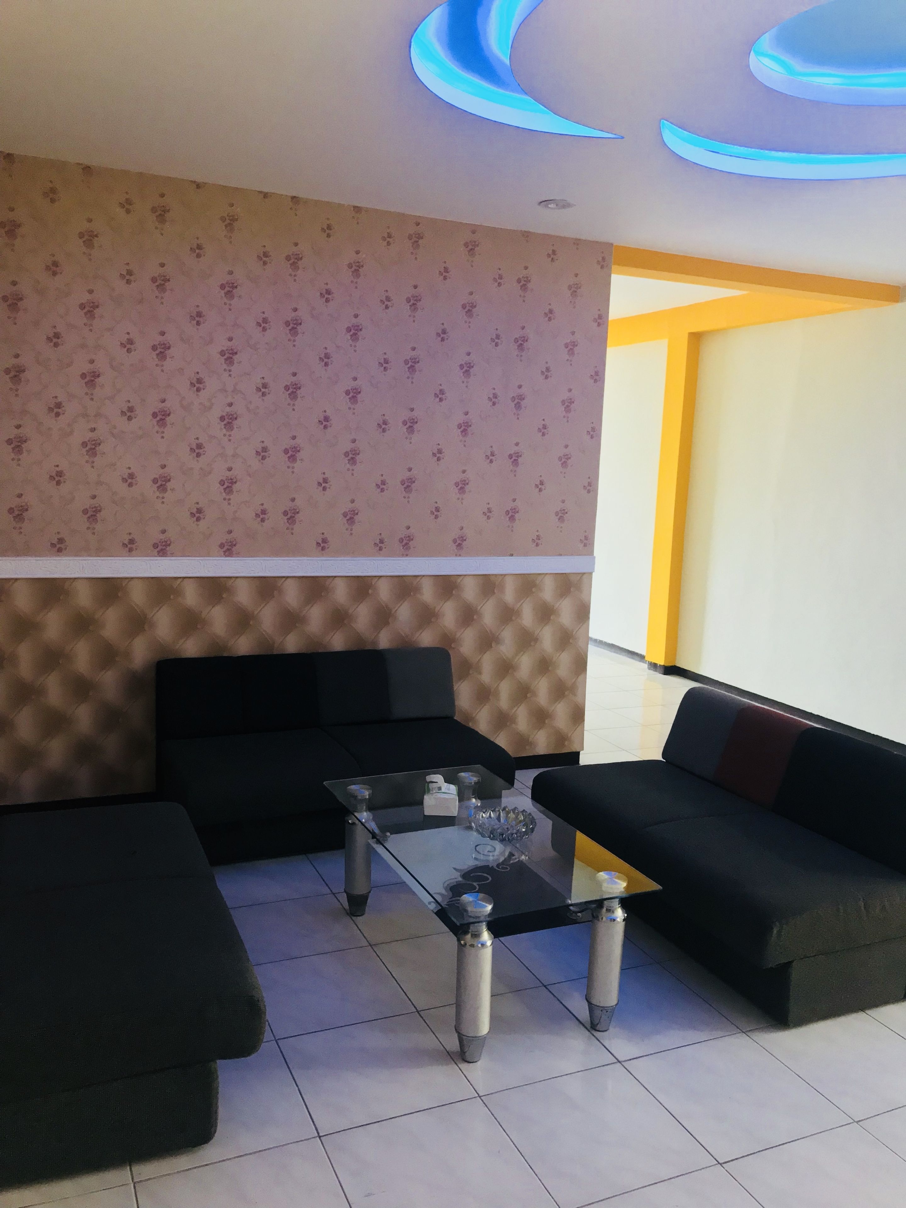 A modern living room with a sofa set, a glass coffee table, and a patterned wallpaper.