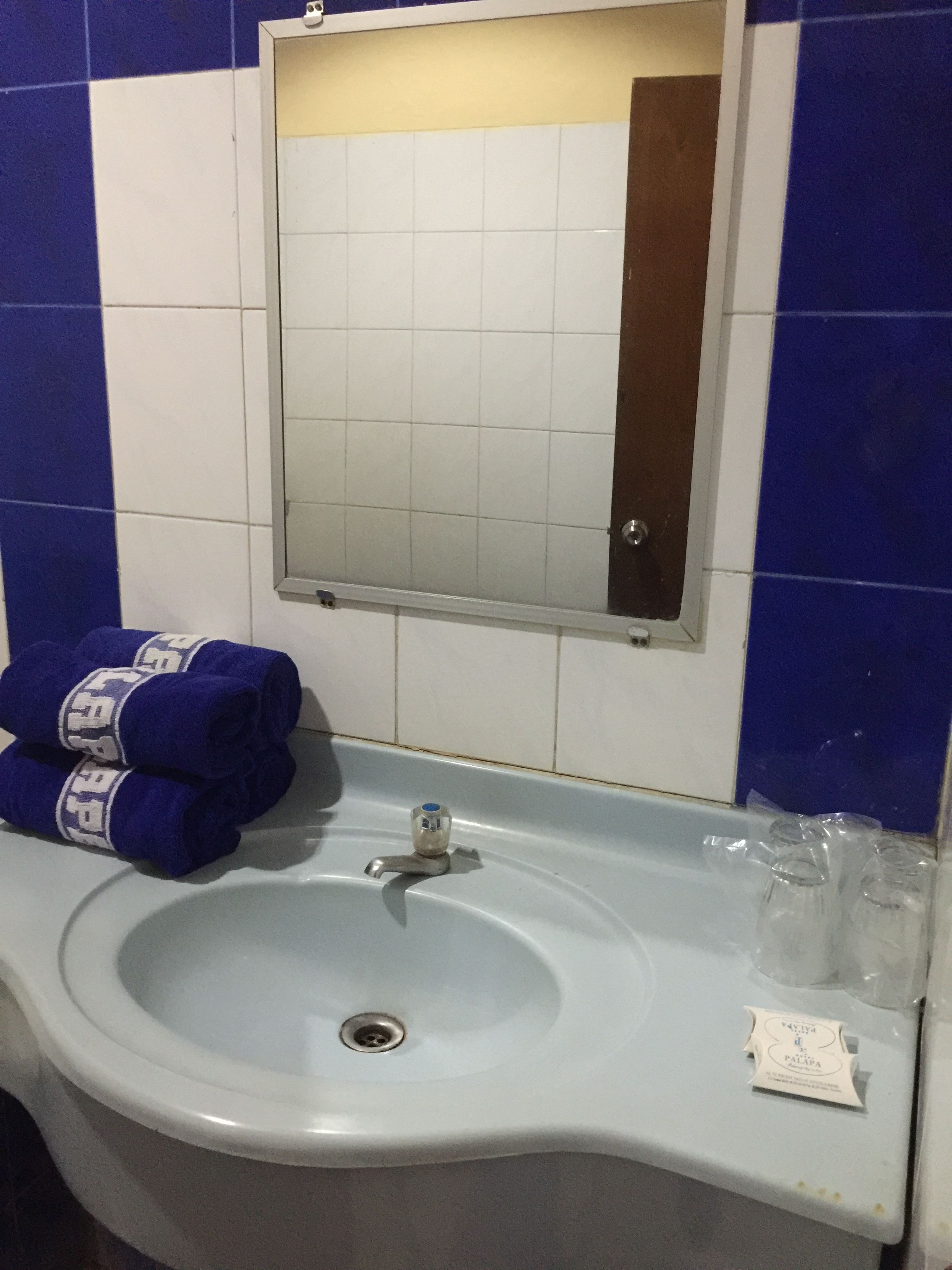 A bathroom sink with a mirror above it, a towel rack with towels, and a small packet on the sink.