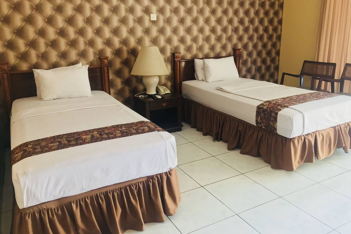 Una habitación de hotel con dos camas, una mesita de noche con lámpara y una silla.