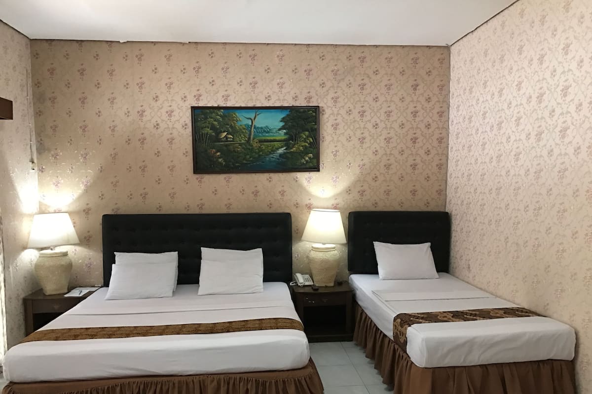 Habitación de hotel con dos camas, cada una con cubrecolchón marrón, almohadas blancas y un cuadro de un paisaje en la pared.