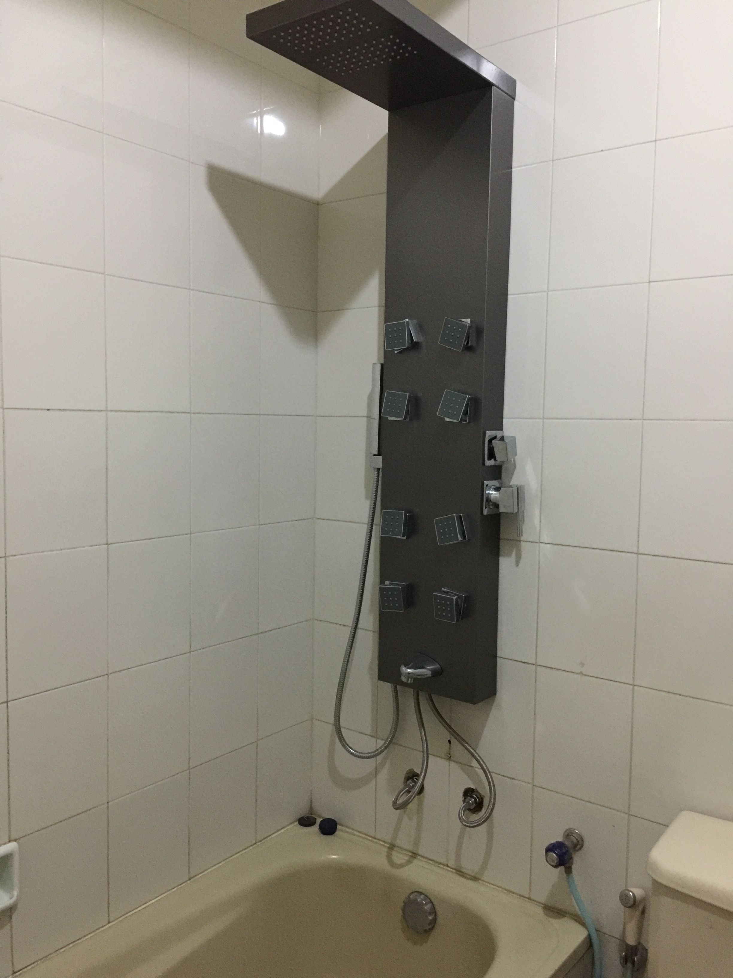 A bathroom with a shower unit mounted on the wall, a bathtub, and a toilet.