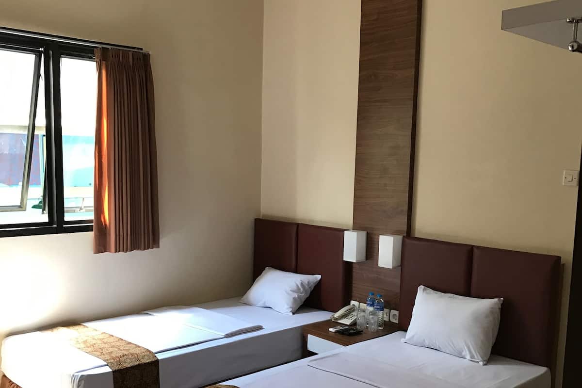 Habitación de hotel con dos camas, una ventana con cortinas, un equipo de aire acondicionado y una mesita de noche con un teléfono y botellas de agua.
