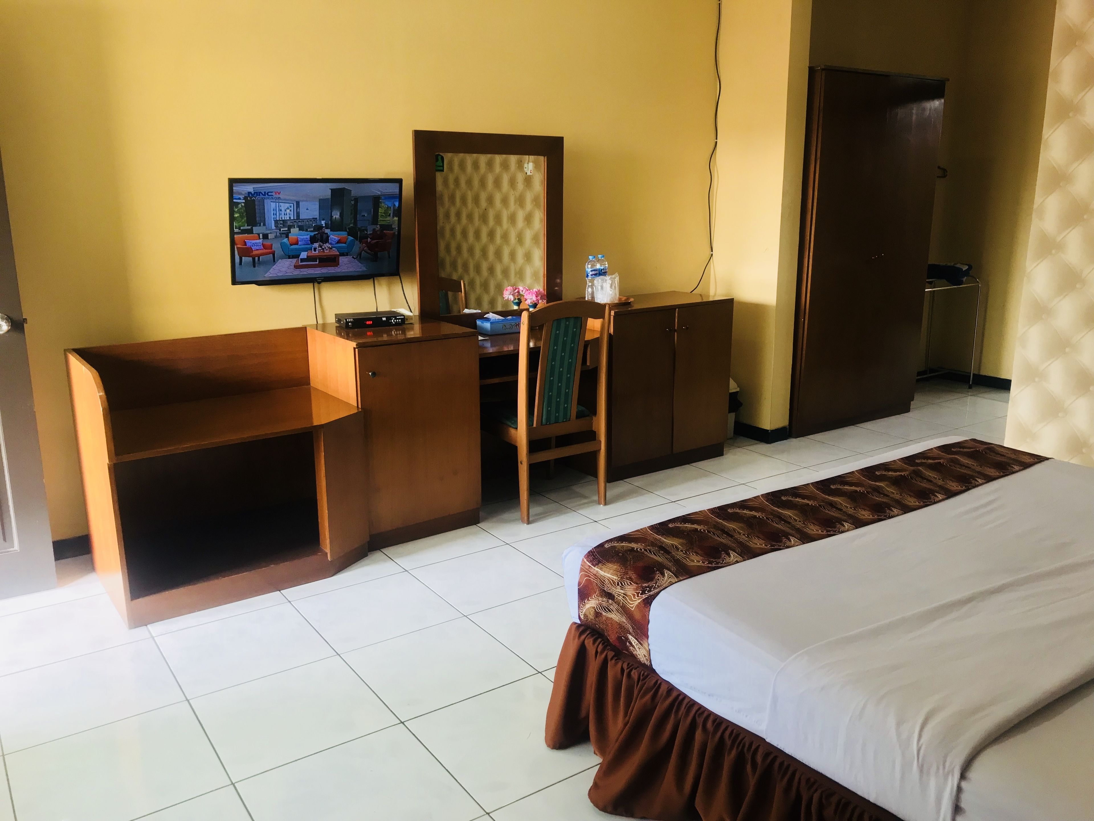 A hotel room with a bed, a desk, a chair, a television, and a wardrobe.
