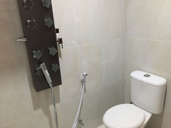 Un baño pequeño y moderno con inodoro blanco, ducha con múltiples cabezales y panel de control en la pared.