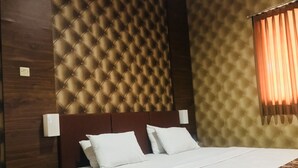 Une chambre d’hôtel avec une tête de lit capitonnée, un lit recouvert de draps blancs, une table de chevet avec un téléphone et un tapis à motifs.