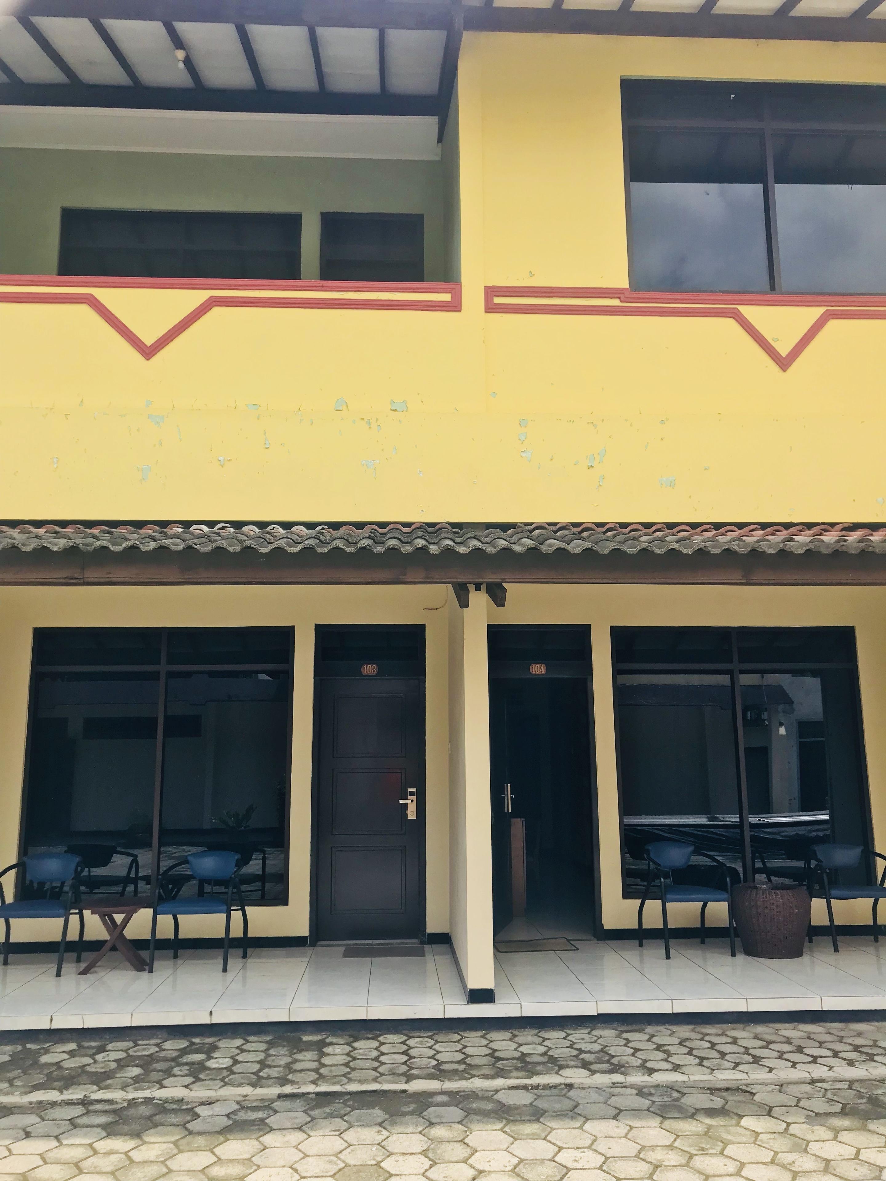 A two-story building with a yellow facade, large windows, and a tiled entrance area with seating.