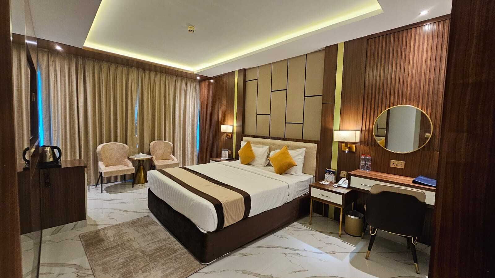 A hotel room with a large bed, a desk, a chair, a mirror, and a TV.