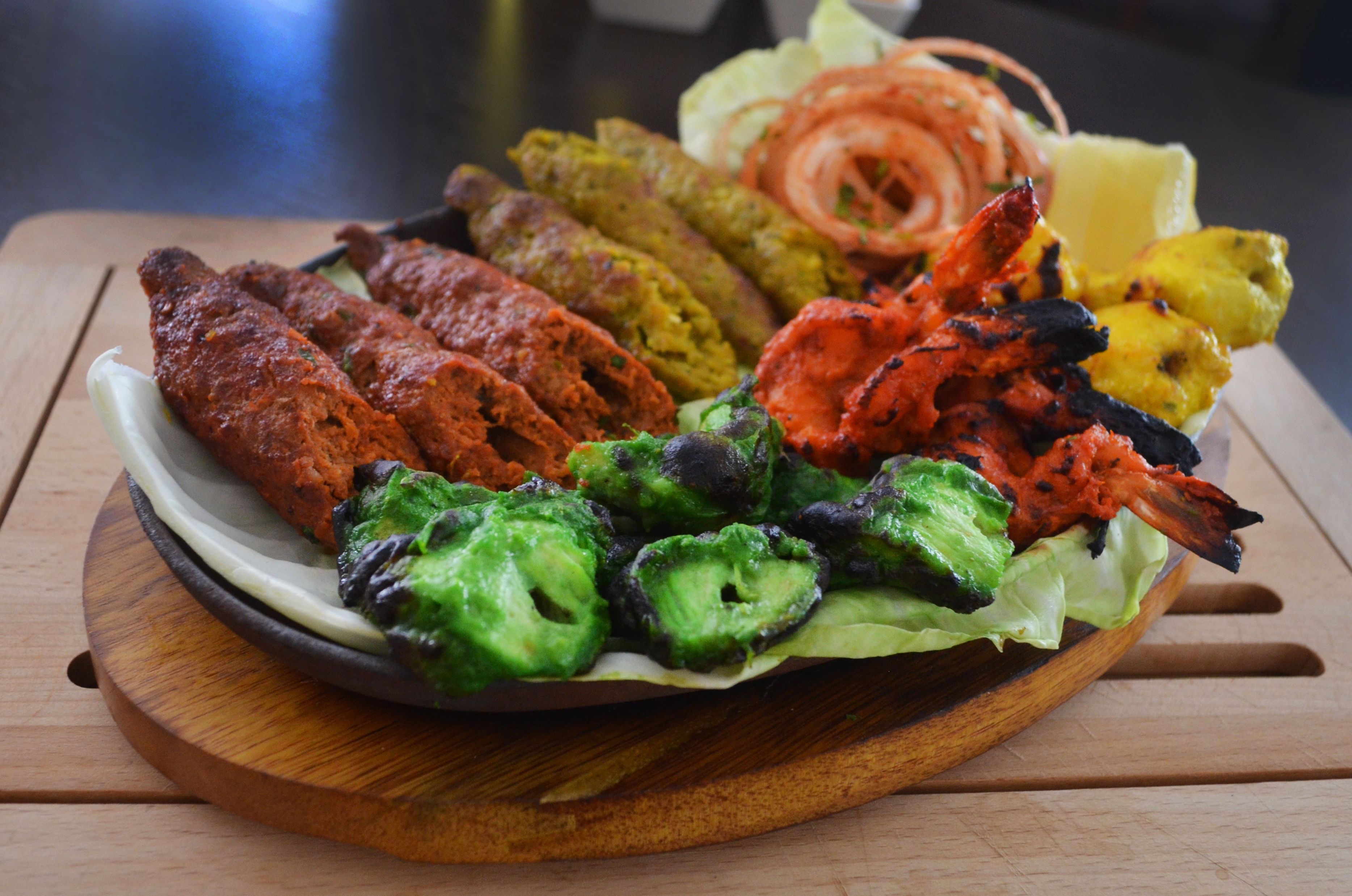 A plate of grilled vegetables and meats on a wooden board.