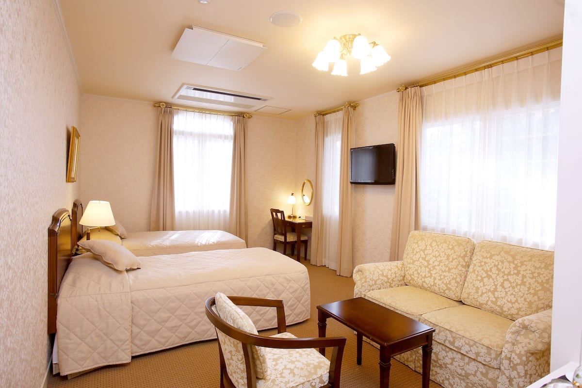 Camera d'albergo con due letti, una poltrona, una scrivania e una televisione.