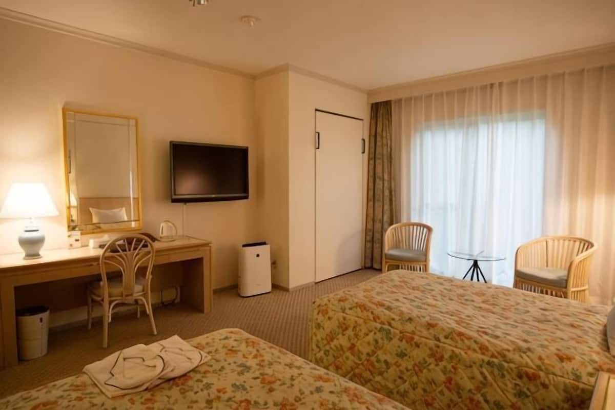 Una camera d'albergo con un letto, una scrivania con una sedia, una televisione e una finestra con tende.