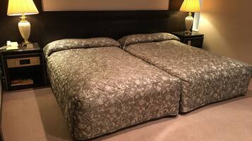A double bed with a floral patterned bedspread, two bedside tables with lamps, a nightstand with a phone and books, and a dark headboard.