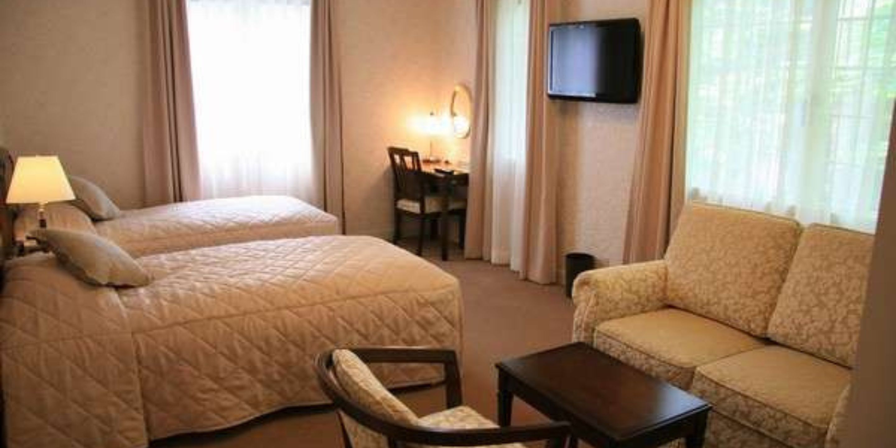 A hotel room with a bed, a sofa, a desk with a chair, and a television mounted on the wall.