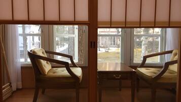 A room with two wooden chairs and a small table, a large window with a view of a snowy outdoor area.
