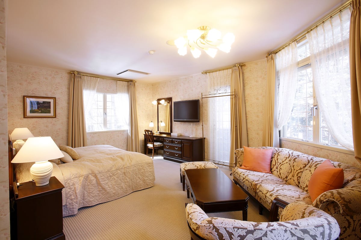 Una camera d'albergo con un letto, un divano, una scrivania, uno specchio e una televisione.
