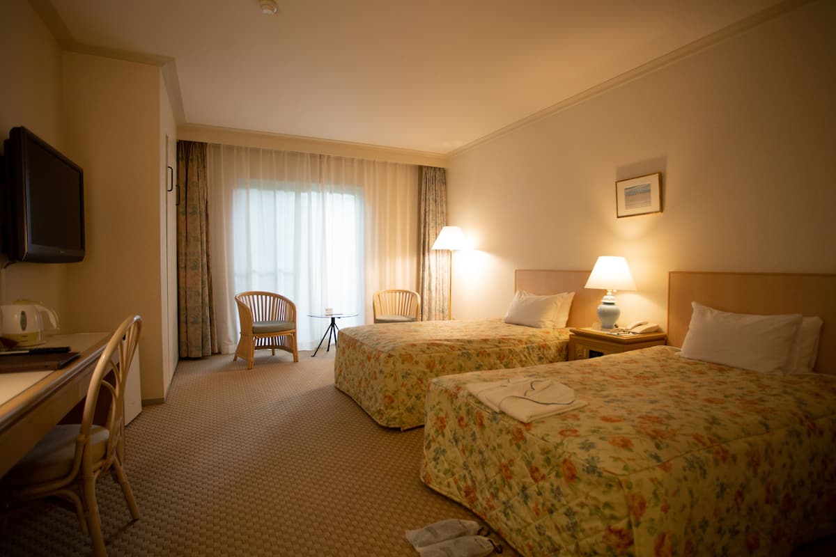 Una camera d'albergo con due letti, una scrivania, una sedia, una televisione e una finestra con tende.