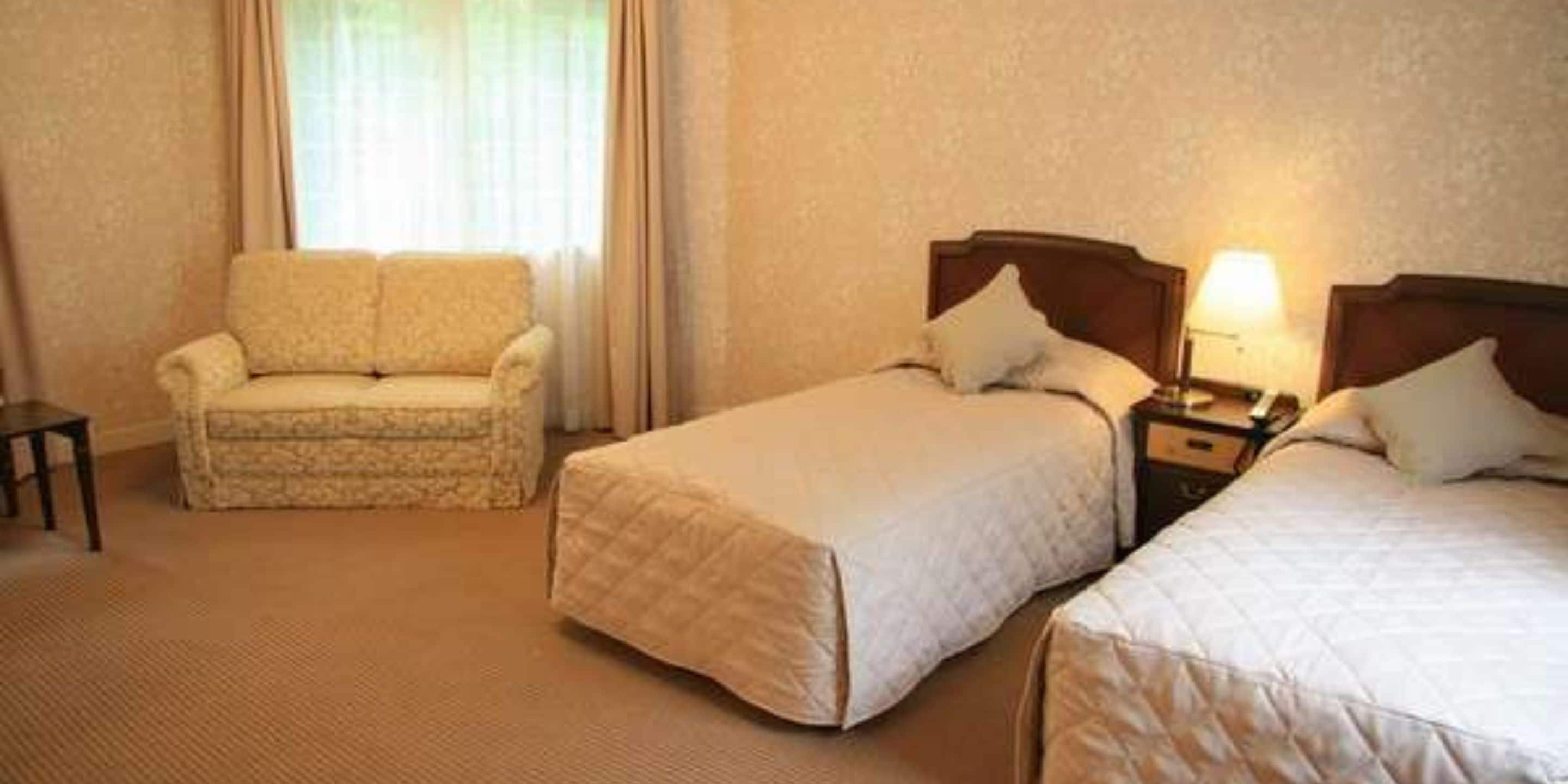 A hotel room with two beds, a sofa, and a nightstand with a lamp.