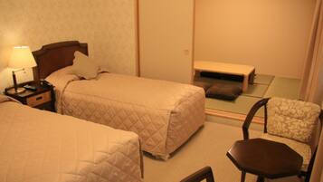 A hotel room with two beds, a nightstand with a lamp, a chair, and a small table.