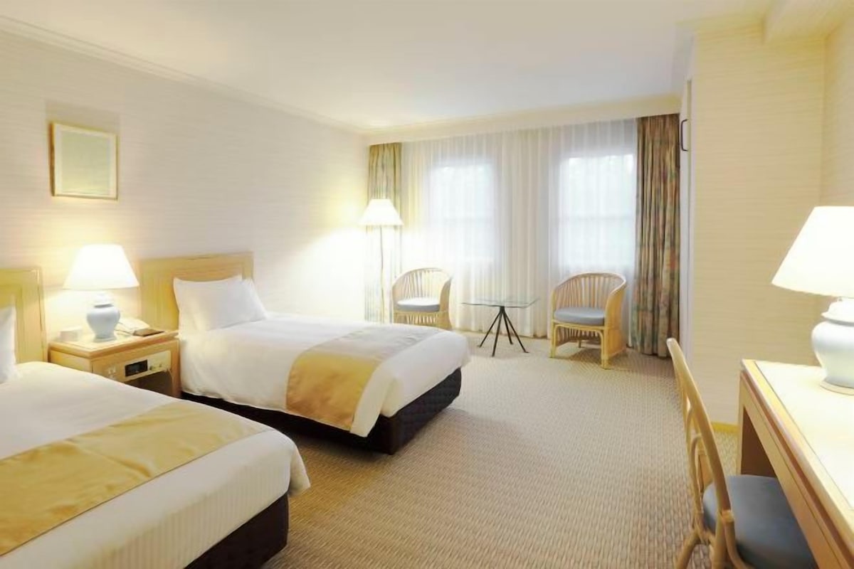 A hotel room with two beds, a desk, a chair, and a small table.