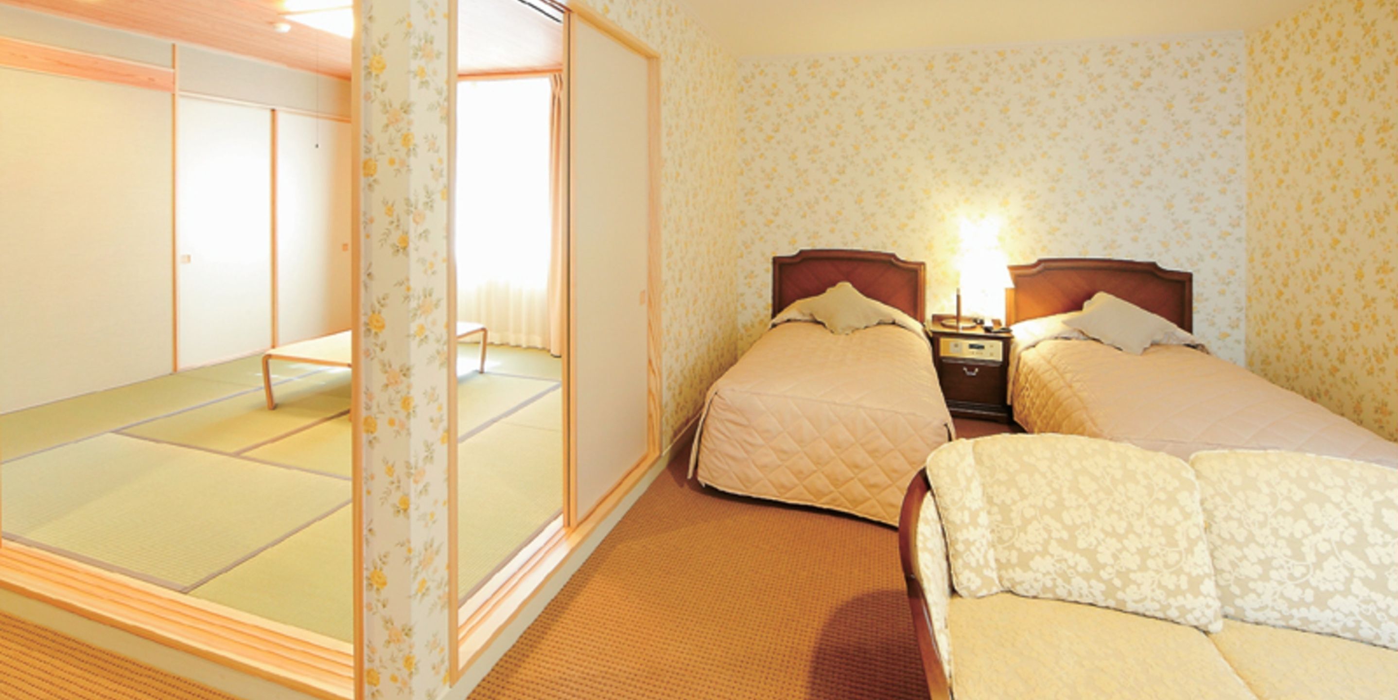 A hotel room with two beds, a wooden floor, and a sliding door leading to a tatami mat area.