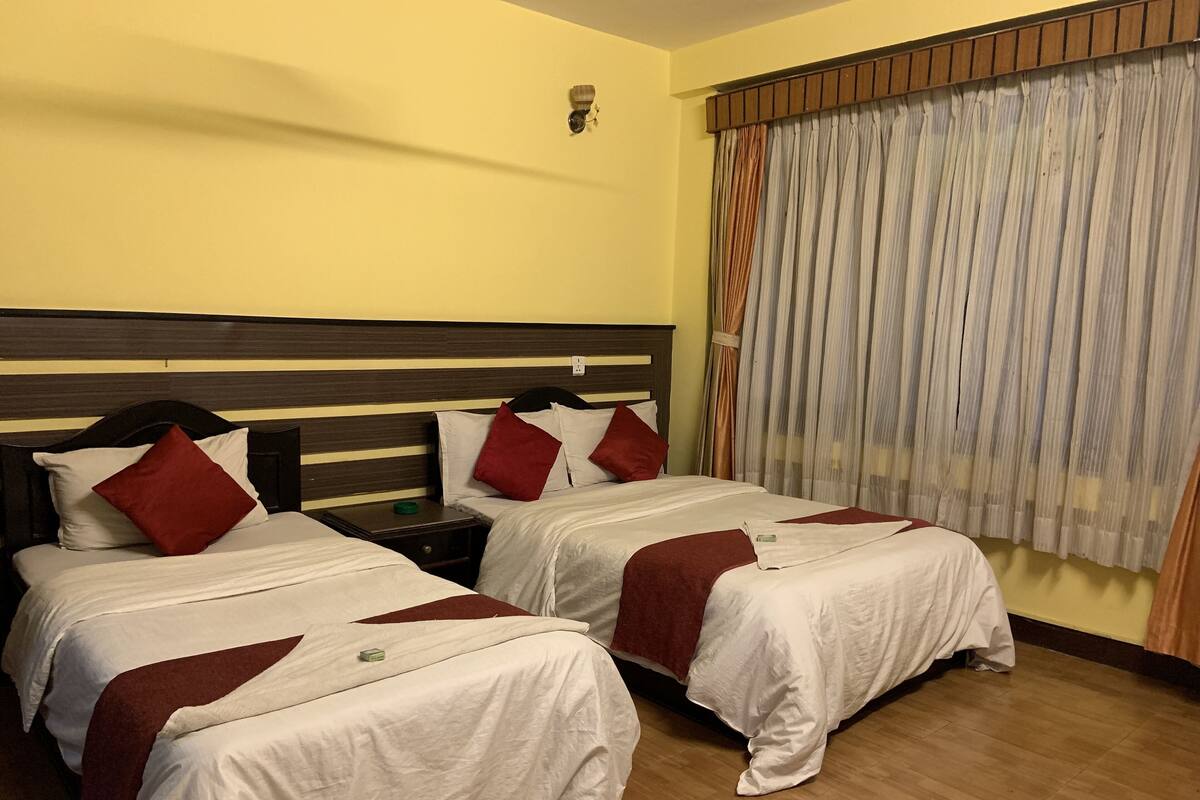 A hotel room with two beds, wooden headboards, white bedding, red pillows, a nightstand, and a window with curtains.