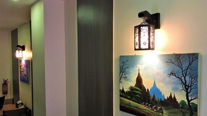 Un pasillo con comedor, un cuadro de un templo y una lámpara fijada a la pared.