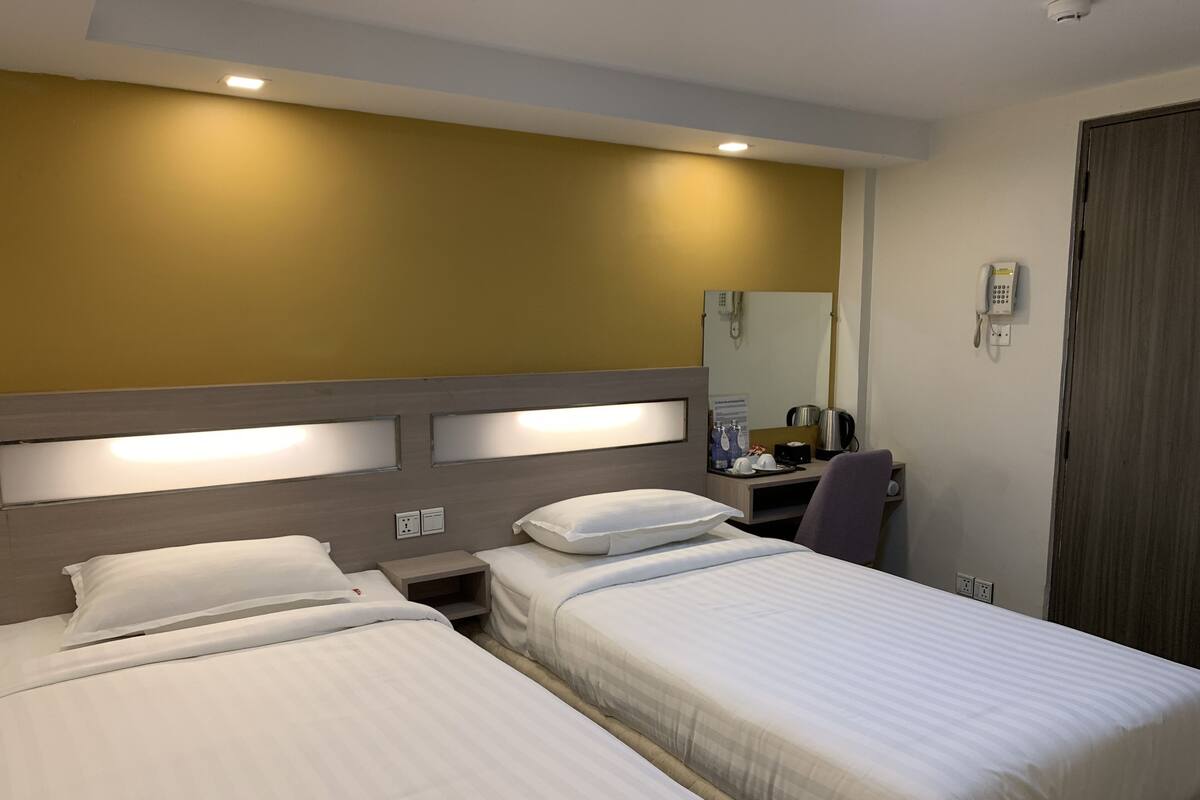 Ein Hotelzimmer mit zwei Einzelbetten, einem Schreibtisch mit Stuhl, einem Telefon und einem Spiegel an der Wand.