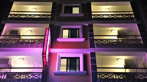 Un edificio de varios pisos con balcones, unidades de aire acondicionado y ventanas iluminadas.