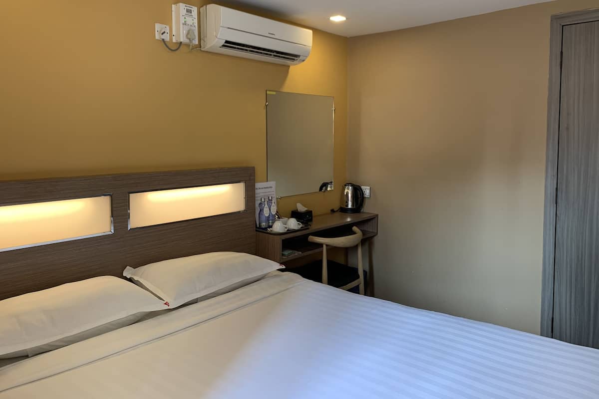 Ein Hotelzimmer mit einem Bett, einem Nachttisch mit Spiegel, einem Waschbecken und einer Klimaanlage.