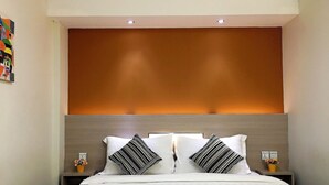 Una habitación de hotel con una cama, dos mesitas de noche y una lámpara fijada a la pared.