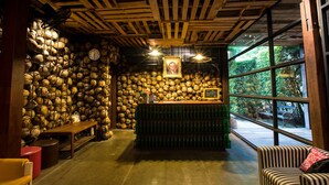 A rustic interior with a wooden ceiling, a wall of stacked coconuts, a bar area with bottles, and a bench.