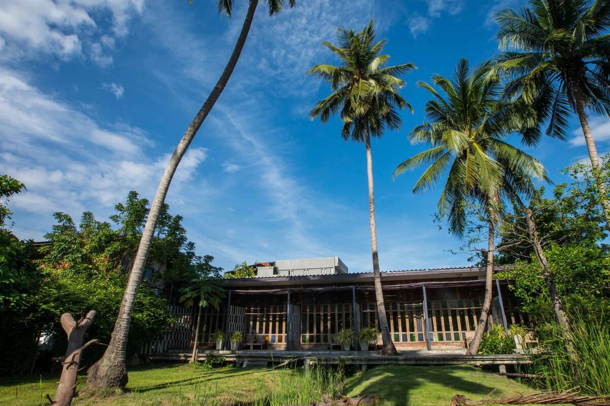 A house with a covered porch, surrounded by palm trees and lush greenery.
