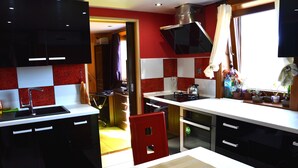 A kitchen with black cabinets, a red chair, and a window with curtains. - MSC Apartments Honeymoon (Zakopane)