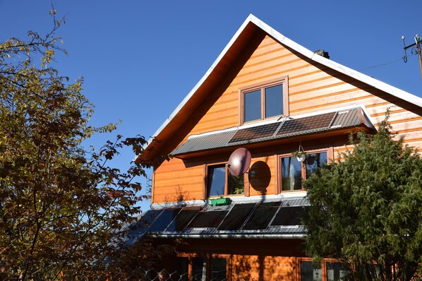 A wooden cabin with a sloped roof, solar panels, and a large window.