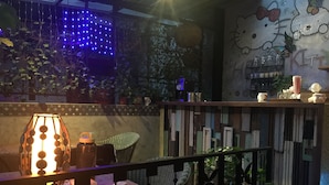 A dimly lit outdoor seating area with a table lamp, wicker chairs, and a decorative wall with Hello Kitty motifs. - Hualien Paris Home B&B (Hualien City)