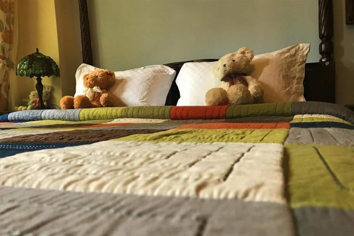 Una cama con colcha, almohadas y un osito de peluche.