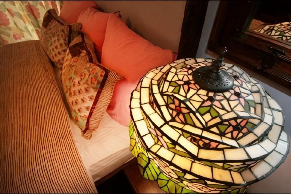 A bed with patterned pillows, a woven headboard, and a mosaic-style lamp.