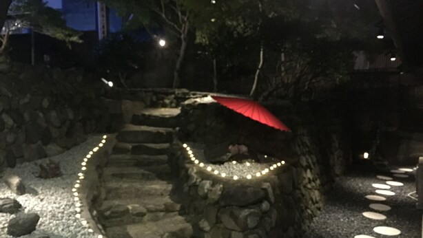 A stone pathway with circular stepping stones, a red umbrella, and string lights. - Wakayama Guest House Shido (Hashimoto)