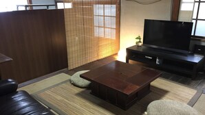 A living room with a dark brown sofa, a wooden coffee table, and a flat-screen TV on a black stand. - Wakayama Guest House Shido (Hashimoto)