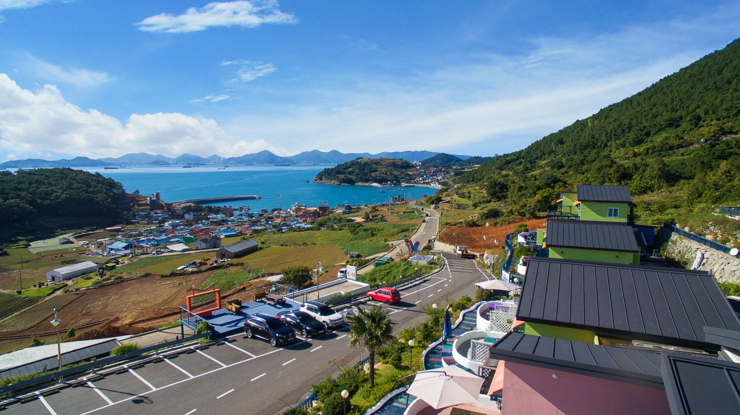 Une ville côtière dotée d’un parking, de bâtiments et offrant une vue sur la mer et les montagnes.