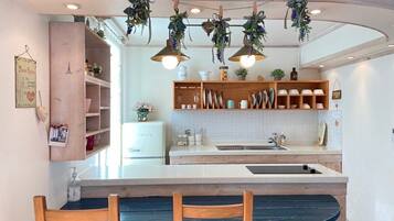 Uma cozinha com ilha central, cadeiras de madeira, plantas penduradas e diversos utensílios.