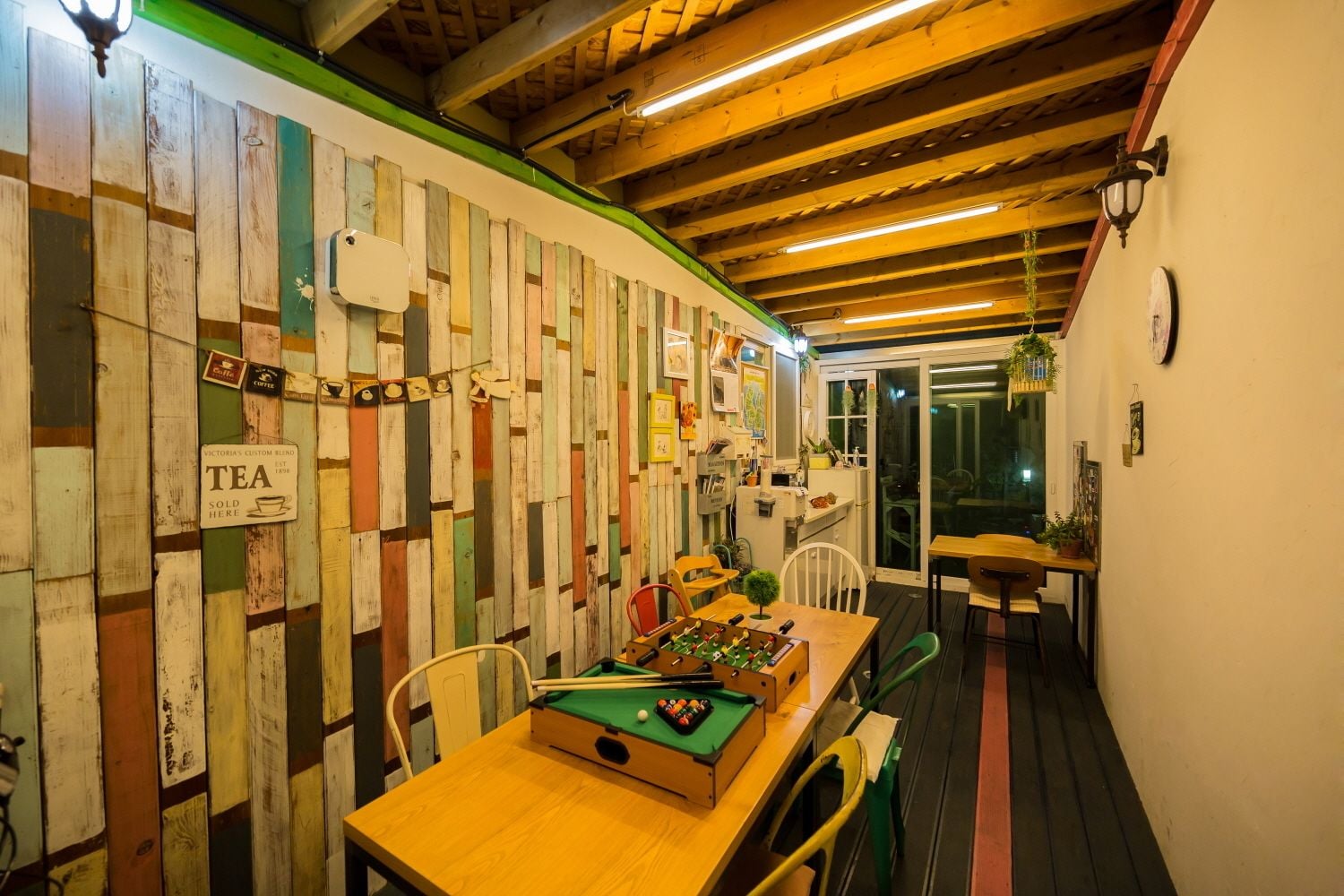 A cozy room with a pool table, wooden walls, and a green-lit ceiling.