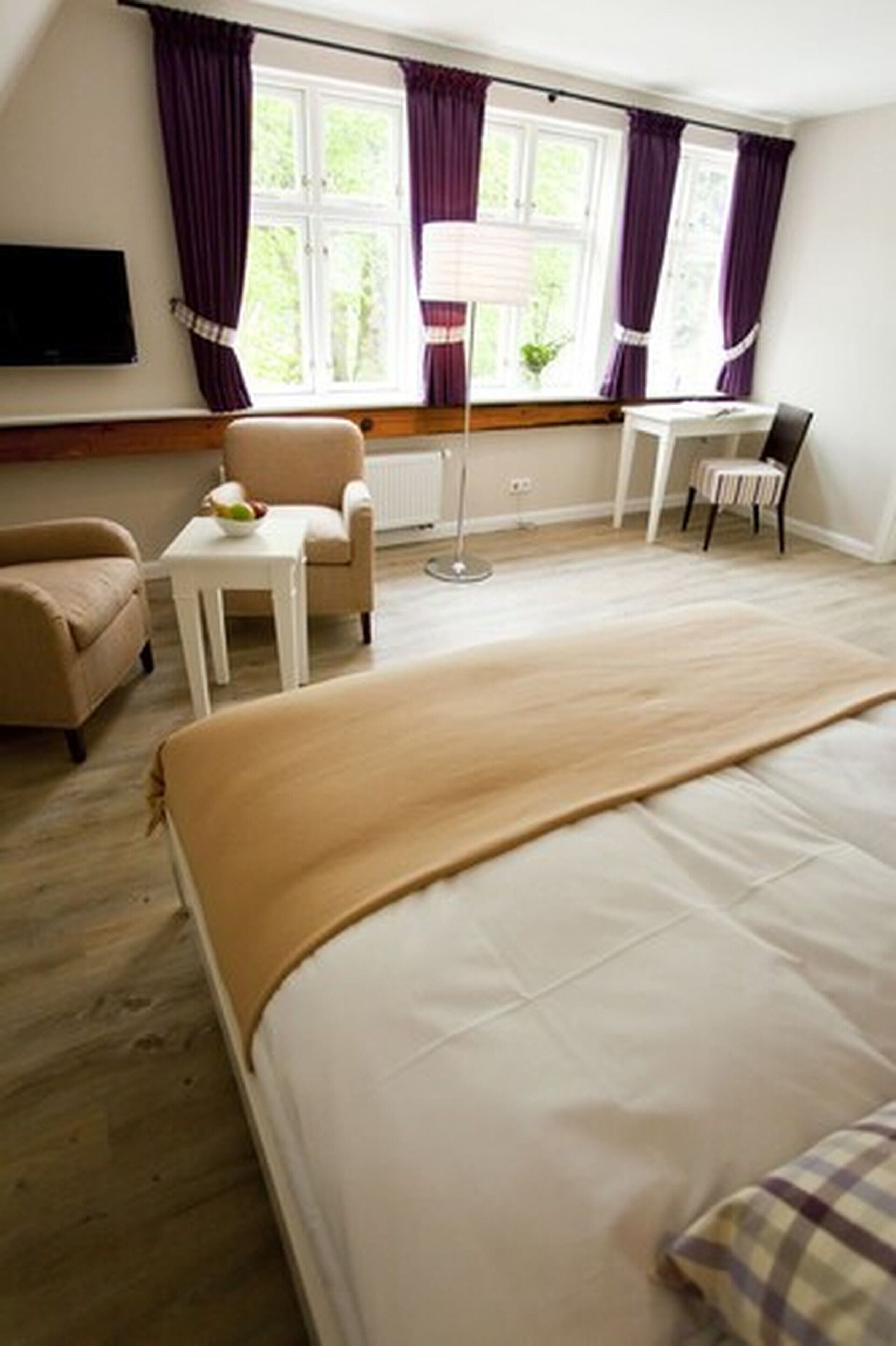 A hotel room with a bed, a chair, a small table, a lamp, and a window with curtains.