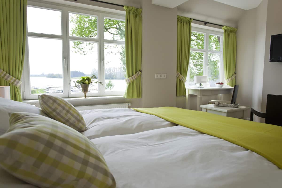 Habitación de hotel con una cama grande, una mesita de noche con lámpara, una ventana con cortinas y vistas al exterior.