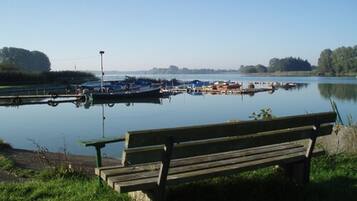 Ein ruhiger See mit vertäuten Booten, einer hölzernen Bank und blauem Himmel.